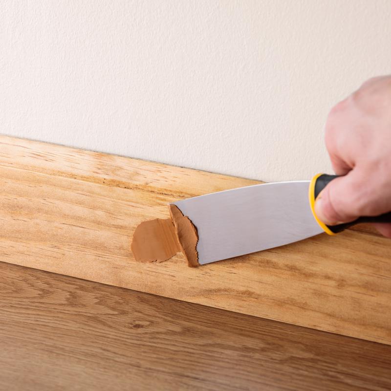 Minwax Wood Putty being applied with a putty knife on a baseboard.