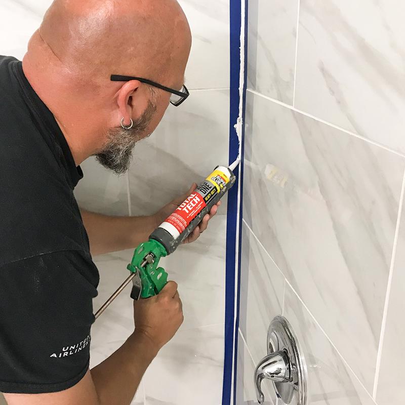 The Original Super Glue Total Tech Construction Adhesive Sealant being applied in the corner of a shower.