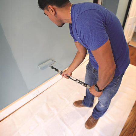 Man standing on a Trimaco Smart Grip Drop Cloth to painting a wall with a roller.