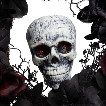 Skull with red eyes surrounded by dark foliage and flowers on a white background