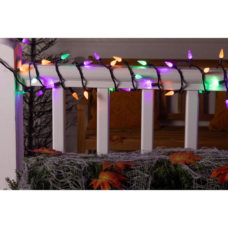 Colorful string lights on a white pergola with Halloween decorations below.