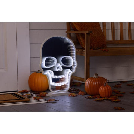 Skull-shaped decorative light with pumpkins and autumn leaves on a porch.