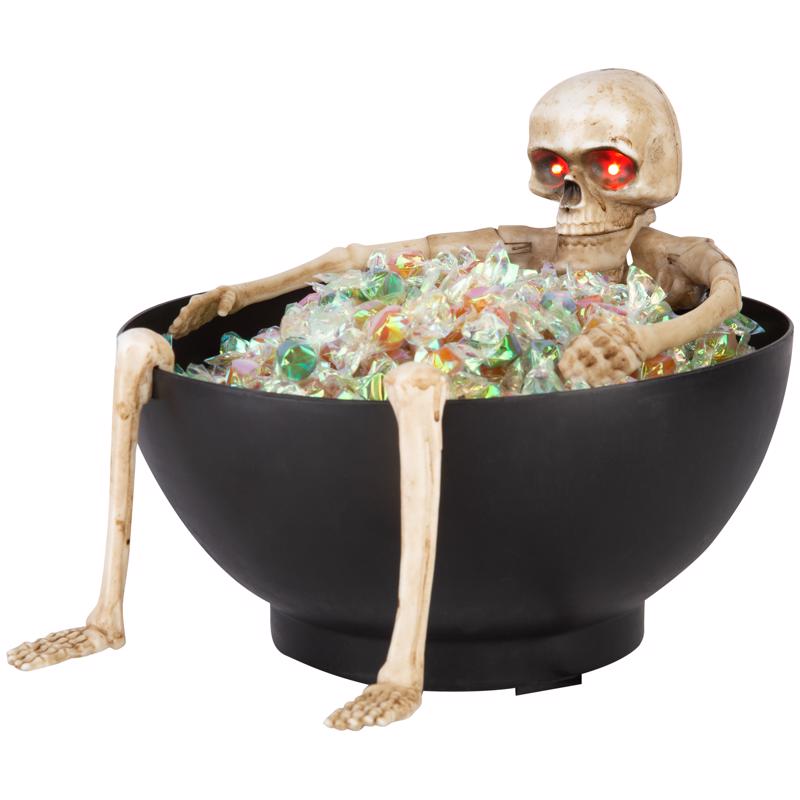 Skeleton figure sitting in a bowl filled with candy on a white background