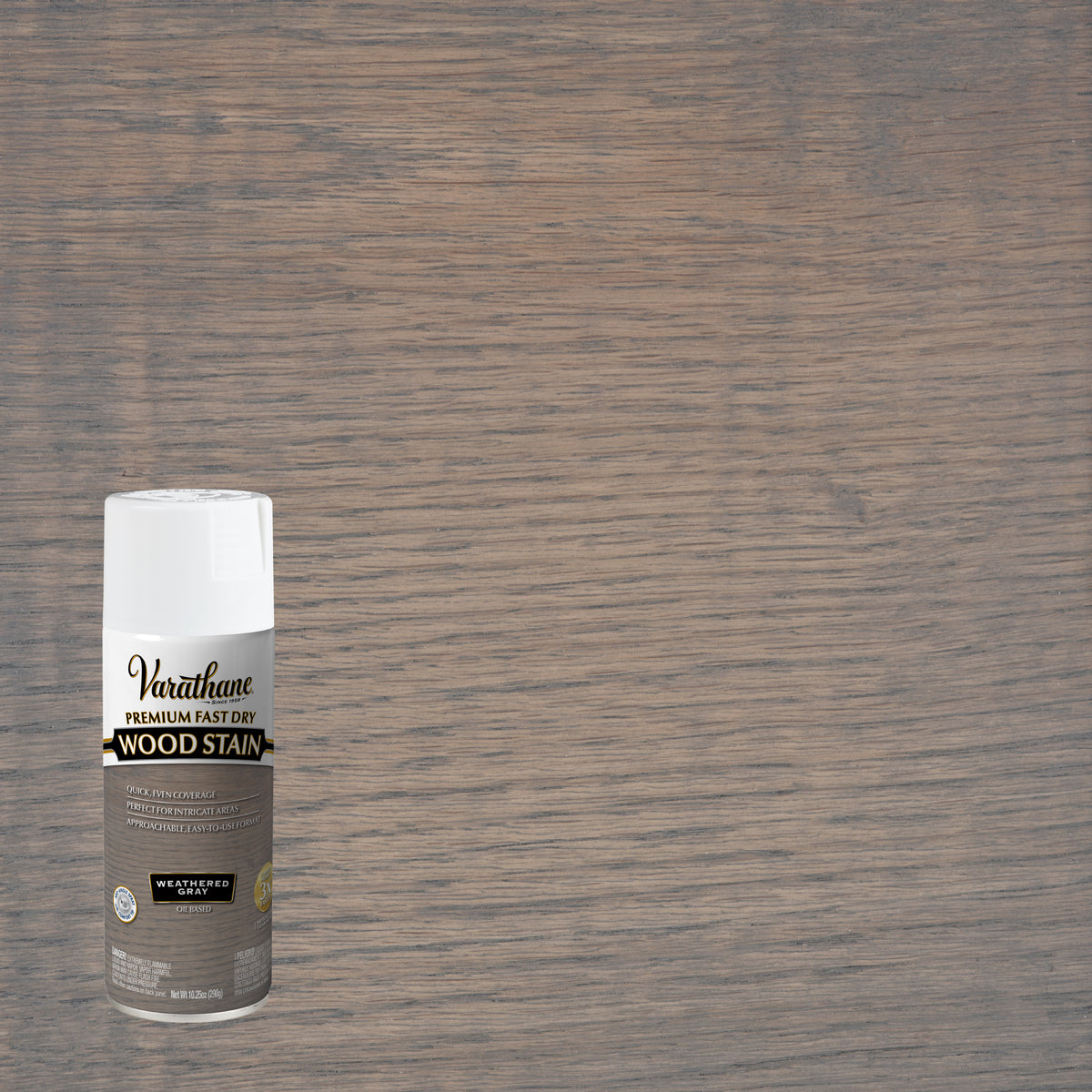 A can of Varathose wood stain spray in weathered gray shown against a large wood grain surface swatch, indicating a brownish gray stain color.