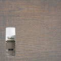 A can of Varathose wood stain spray in weathered gray shown against a large wood grain surface swatch, indicating a brownish gray stain color.