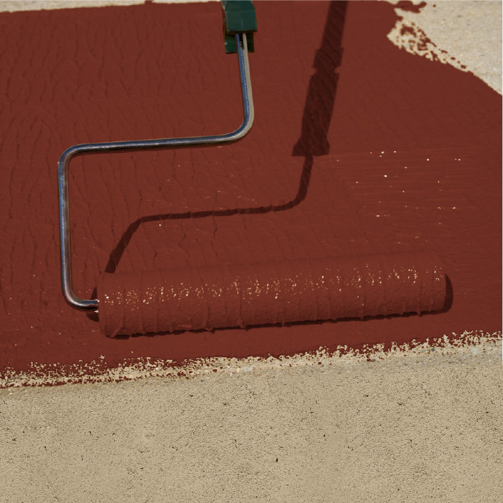 A paint roller covered in reddish-brown paint applies a coat to a beige surface, with the roller handle extending toward the top edge.