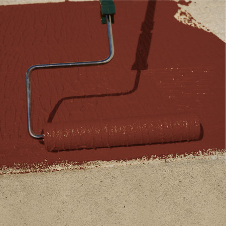 A paint roller covered in reddish-brown paint applies a coat to a beige surface, with the roller handle extending toward the top edge.