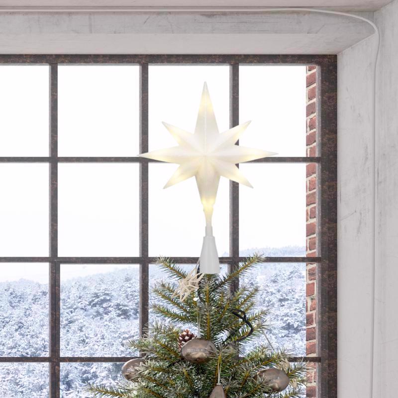 Decorative star light on a Christmas tree with a snowy landscape view through a window.