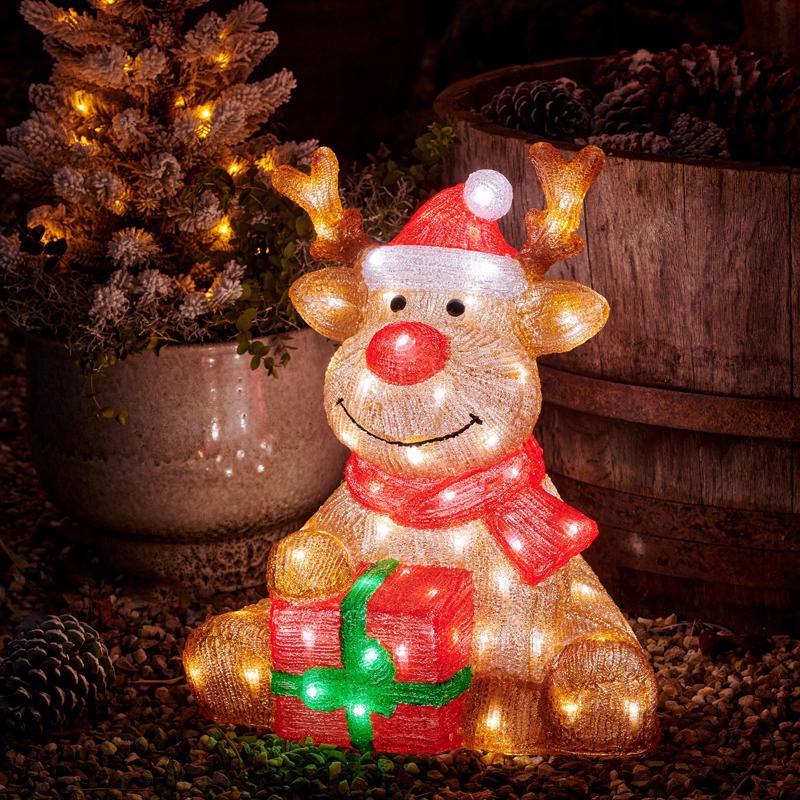 Decorative reindeer figure with lights, Santa hat, and red scarf in a festive setting.
