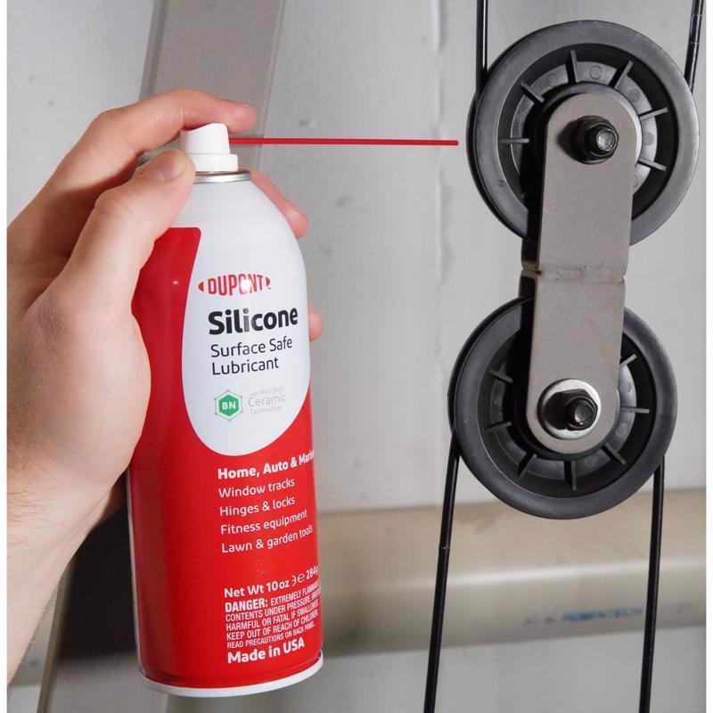 Hand holding a can of Dupont silicone lubricant near a window track.