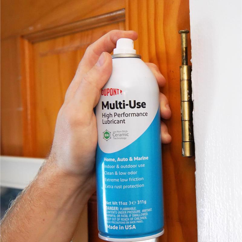 Hand holding a DuPont Multi-Use High Performance Lubricant can in front of a wooden door.