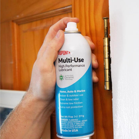 Hand holding a DuPont Multi-Use High Performance Lubricant can in front of a wooden door.