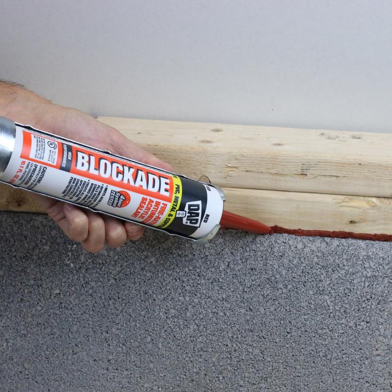 DAP 10.1 Oz Blockade High Performance Intumescent Acrylic Sealant being applied to gap at floor between wood and concrete.