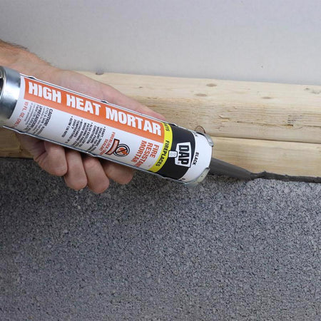 DAP 10 Oz Black High Heat Mortar being applied at gap between wood and concrete.