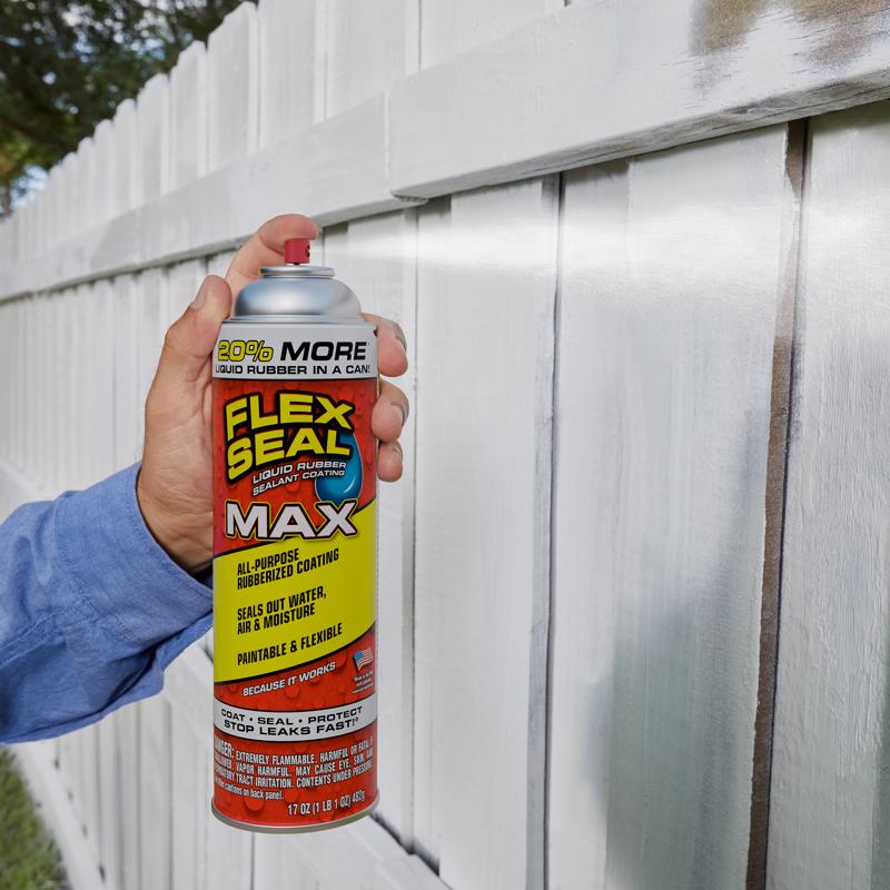 Person holding a Flex Seal MAX can against a white fence.