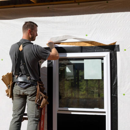 Person installing a window in a building under construction using frog tape pro flashing tape