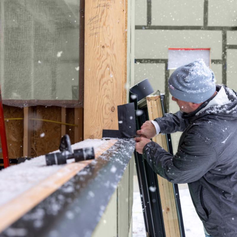 Person installing a door in a construction setting using frog tape pro flashing tape with snow falling