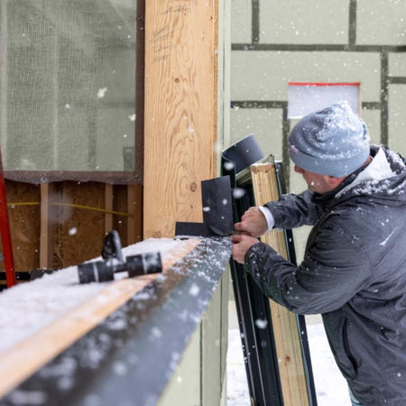 Person installing a door in a construction setting using frog tape pro flashing tape with snow falling