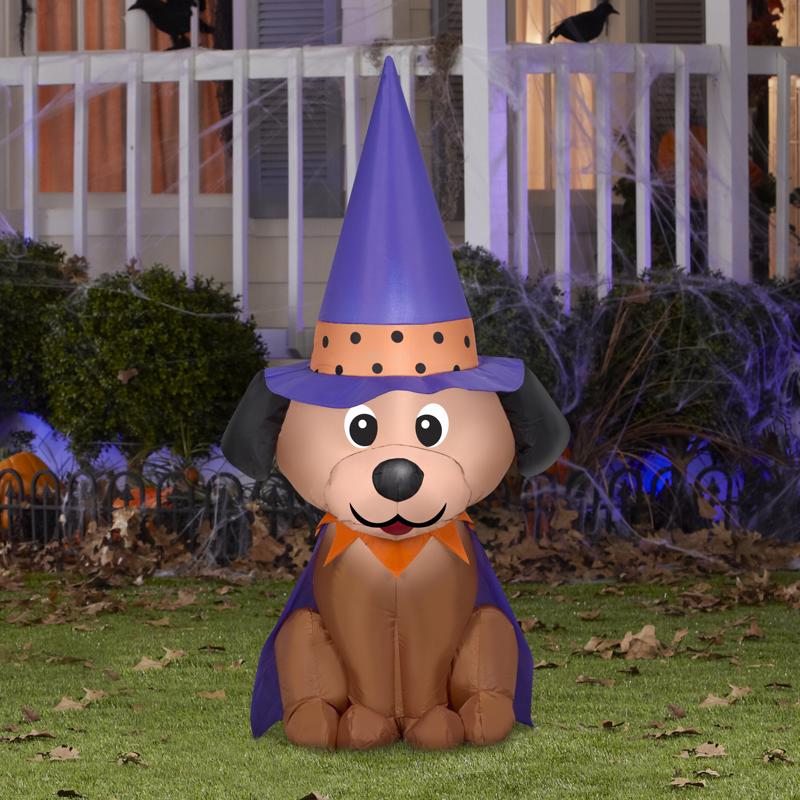 Inflatable dog with a purple witch hat and cape on a grassy lawn.