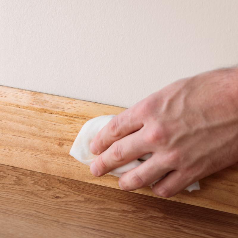 Wiping away excess Minwax 1 Lb Wood Putty from a baseboard.