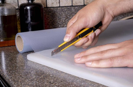 Person cutting a roll of paper with a OLFA 9mm A-1 Auto-Lock Precision Utility Knife on a kitchen counter.