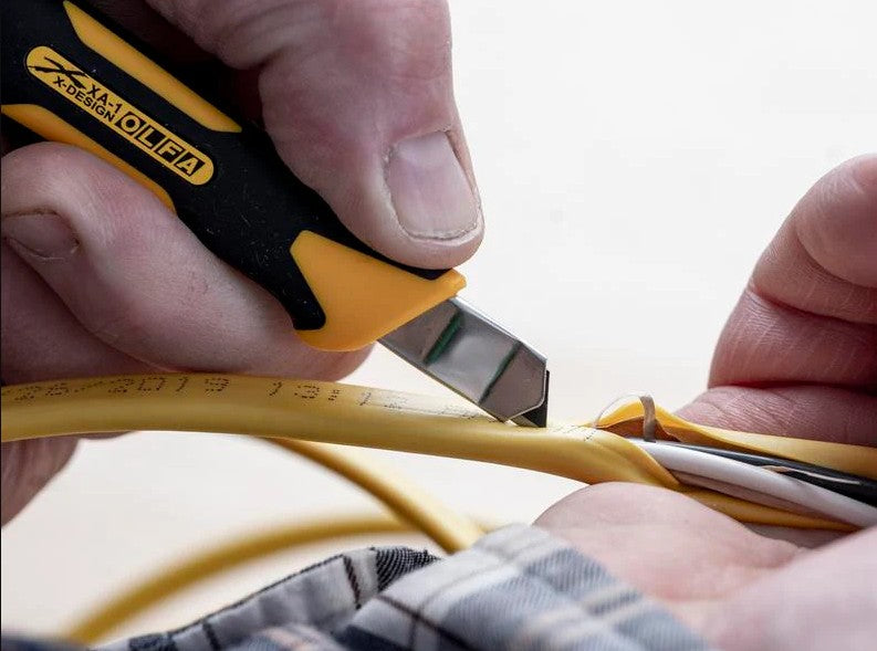 Person using the OLFA 9mm XA-1 Fiberglass Precision Knife to cut yellow cable with a blurred background
