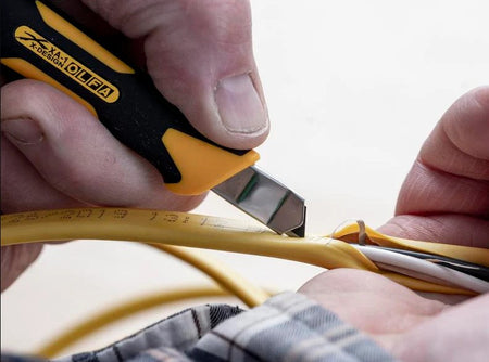 Person using the OLFA 9mm XA-1 Fiberglass Precision Knife to cut yellow cable with a blurred background