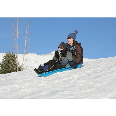 Two people sledding down a snowy hill on a clear day on the Winter Lightning Plastic Sled