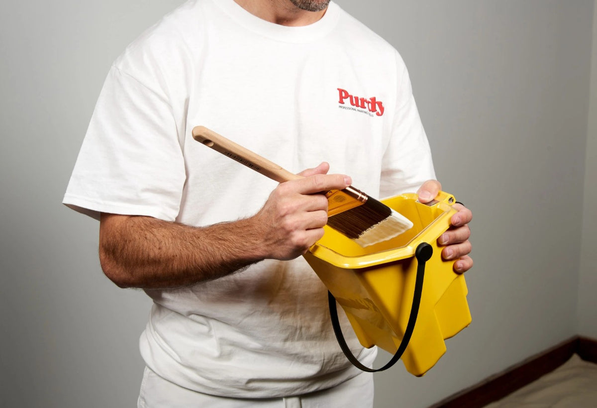 Man holding the Purdy Painter's Pail with a brush with paint on it.