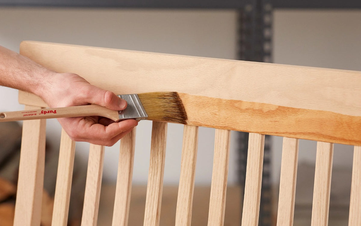 Person painting a wooden chair with a Purdy White Adjutant paint brush