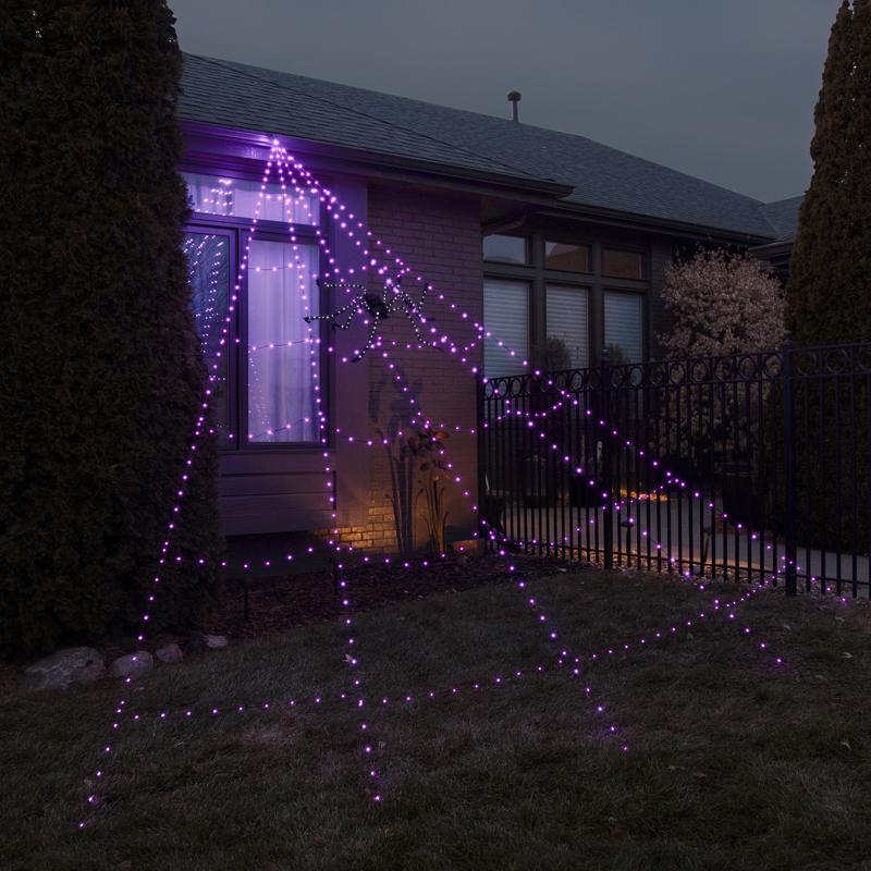 Purple string lights shaped like a spider web in front of a house at night.