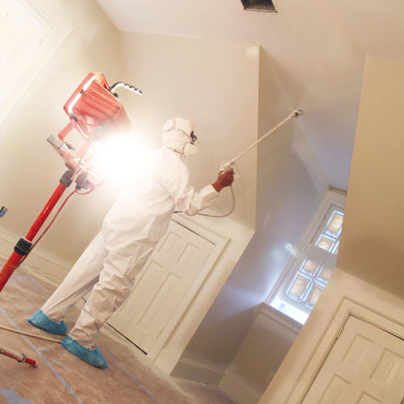 Trimaco Polyolefin Coveralls being worn by a man spraying a ceiling with a paint sprayer.