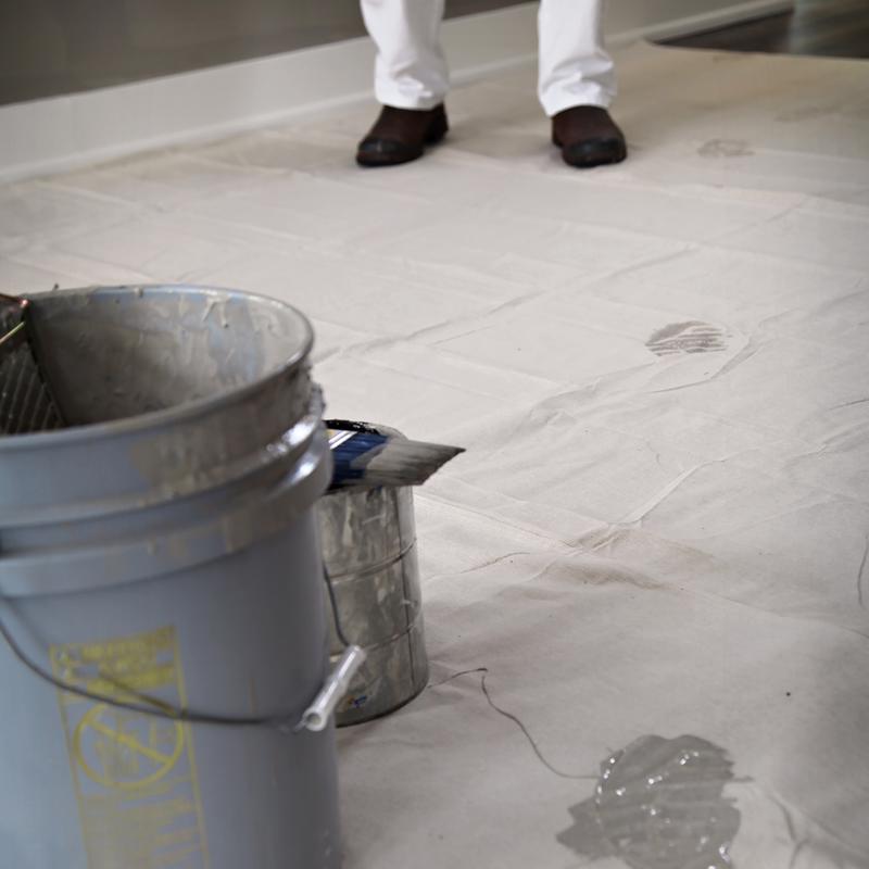 Trimaco Stay Put Canvas Drop Cloth on a floor with a paint can on top of it