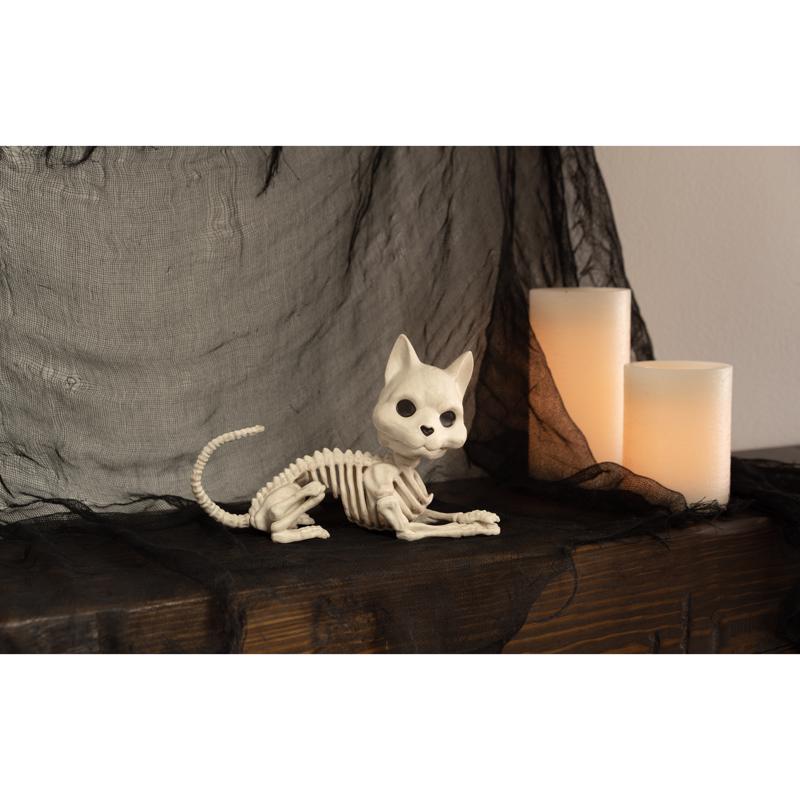 Halloween Skeletal cat figurine on a dark surface with a candle in the background