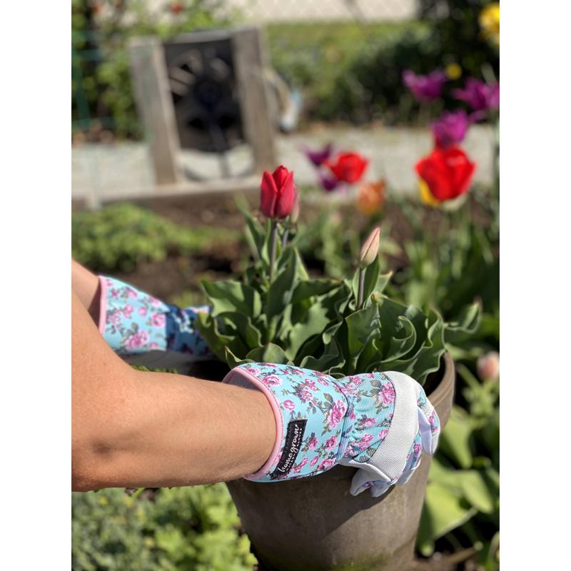 Person wearing floral gardening gloves holding a potted plant with flowers in the background