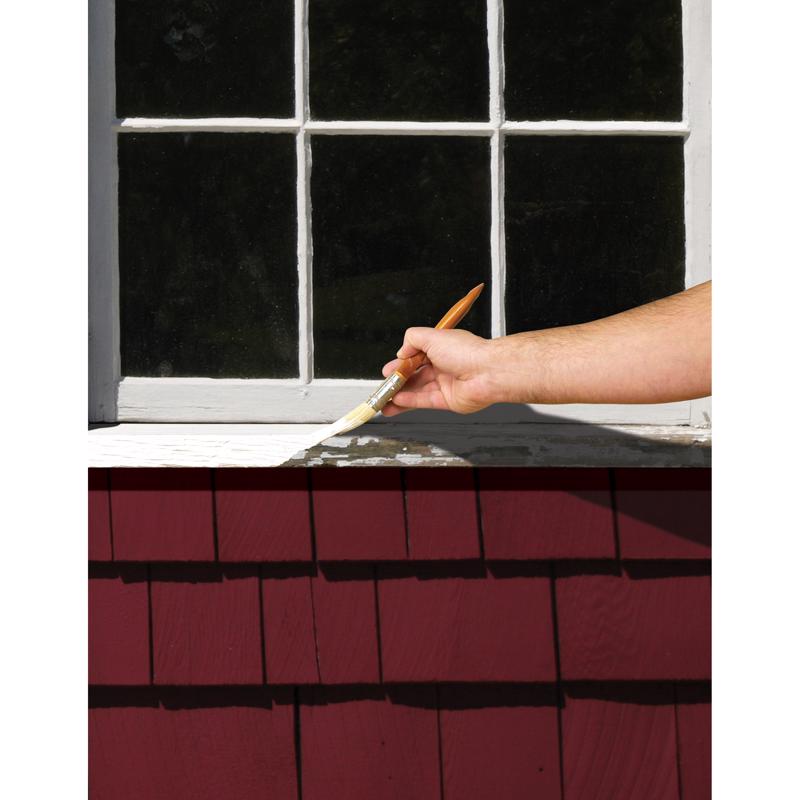 Hand holding a paintbrush applying Zinsser Peel Stop Triple Thick primer around a window in the background.